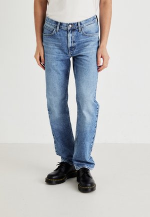 Light blue denim jeans with a straight leg design, five pockets, and a standard waistband. Paired with black lace-up shoes.