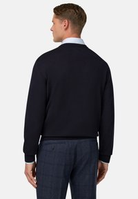 Jūras spēku zilās krāsas džemperis ar V-veida kakla izgriezumu, ribotām piedurknēm un apakšmalu. Apvienots ar zilu biksēm ar rakstu, kurām ir pogu detaļa.