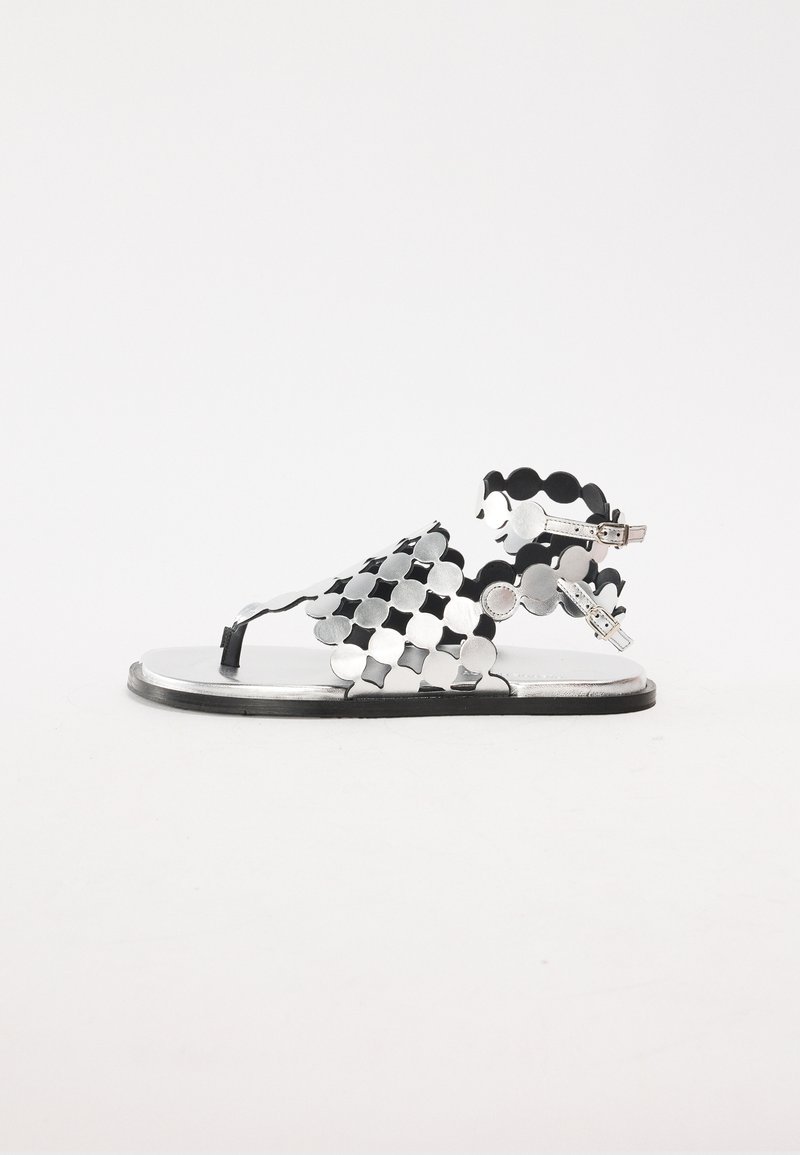 Mustat ja hopeiset litteät sandaalit, joissa on aaltoileva, rei'itetty muotoilu; säädettävät nilkkahihnat; metalliset yksityiskohdat; minimalistinen muoto ja rakenne.