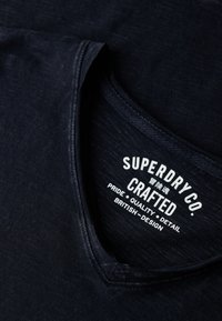Mørkeblå V-hals T-shirt lavet af blødt stof, med et trykt logomærke med "Superdry Co." og kvalitetsdetaljer indvendigt.