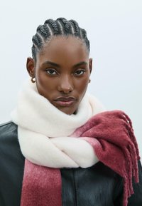 Sciarpa in misto lana con tonalità degradanti di bianco e rosa scuro, con estremità frangiate. Indossata sopra un giubbotto in pelle nera, con una finitura morbida e strutturata.