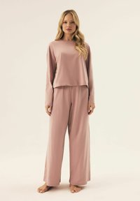Jasnoróżowy zestaw dresowy składający się z krótkiego topu z długim rękawem i szerokich spodni, wykonany z miękkiego materiału dla wygody.