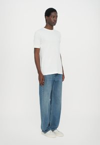 Hvit kortermet t-skjorte kombinert med løstsittende blå denimjeans og hvite joggesko, som skaper en uformell, avslappet silhuett.