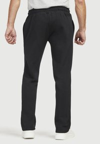 Schwarze Jogginghose aus Baumwollmischung, mit elastischem Bund und Seitentaschen. Die Beine verlaufen leicht zum Knöchel hin und sind mit weißen Sneakers kombiniert.