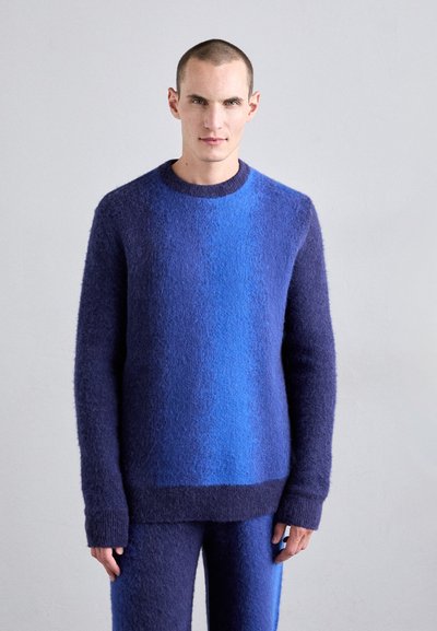 Suéter de punto en degradado azul y púrpura, con textura suave, cuello redondo, mangas largas y corte relajado, acompañado de pantalones a juego.