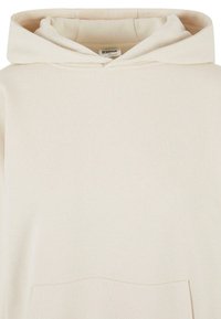 Hettegenser i myk beige stoff, med en frontlomme og en avslappet passform, samt et enkelt design og minimale sømdetaljer.