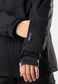Schwarze wasserdichte Jacke mit verstellbaren Manschetten. Mit Klettverschluss, STX 8000-Branding und einem weichen Innenfutter für mehr Komfort.