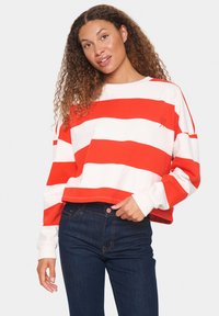 Felpa cropped a righe rosse e bianche con maniche lunghe, caratterizzata da un dettaglio ricamato sul petto, abbinata a jeans blu scuro.