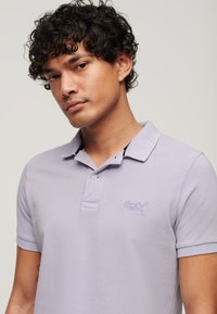 Lila polo-shirt van een gestructureerde stof, korte mouwen, een knoopjessluiting met twee knopen en geborduurd logo-detail op de linkerborst.