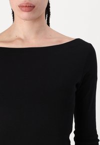 Fekete hosszú ujjú felső széles hajónyakkal, sima anyagból készült, formás siluettel és minimalista dizájnnal.