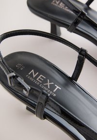 Fekete lakkbőr szandálok vékony pántokkal, enyhe sarokkal, és belső márkajelzés nyomattal. Méret: 6½ (40).