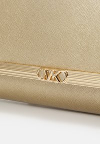 Bolso texturizado en dorado con herrajes dorados que presentan las iniciales "MK" en el centro, acentuado por líneas horizontales arriba y abajo.