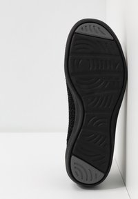 Černá podrážka tenisky s texturovaným gumovým povrchem a vlnitým vzorem, lehký design a nenápadná logo ražba.