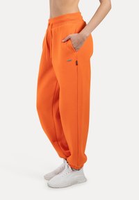 Oranger sweatpants med elastisk talje, sidelommer og ribbede manchetter. Parret med hvide sneakers for et afslappet look.