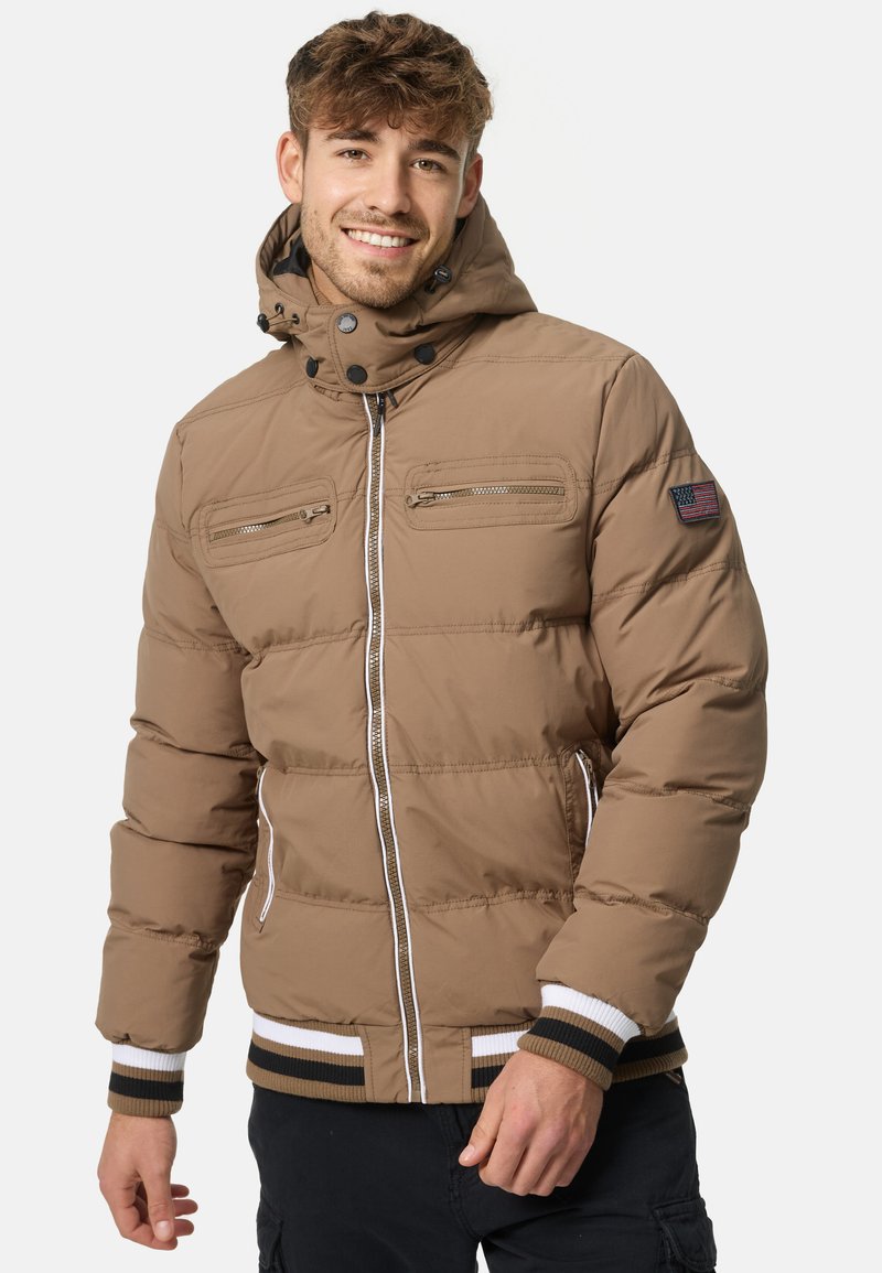 Brown padded jacket with a zip front, two chest pockets, ribbed cuffs, and a hood. Features striped hem and American flag patch on the sleeve.