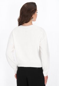 Pulover alb din tricot cu guler rotund, mâneci lungi și manșete fasonate. Textura este moale, cu un finisaj ușor pufos.