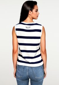 Mouwloze gestreepte tanktop in wit en marineblauw, met een achterkant met een grafisch ontwerp van een hart met vleugels. Het materiaal lijkt zacht en casual.