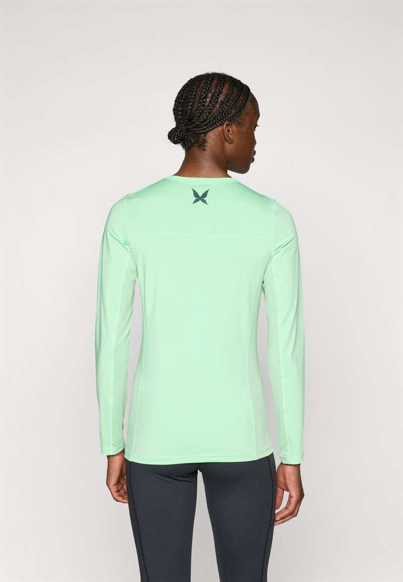 Długi rękaw sportowy top w jasnym miętowym kolorze. Gładki materiał z dopasowanym krojem i stylizowanym logo w ciemnozielonym kolorze na plecach.