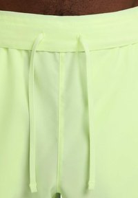 Bañador verde neón con cintura elástica y cordón, textura suave y tela transpirable, mostrando detalles de costura mínimos.