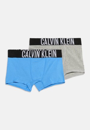 Dva páry chlapčenských boxeriek Calvin Klein, jeden svetlomodrý a jeden svetlosivý, oba s čiernymi páskami na páse a bielymi logami značky.