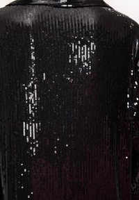 Tissu en sequins noirs avec une finition brillante, présentant une surface texturée couverte de petits disques réfléchissants disposés de manière rapprochée.