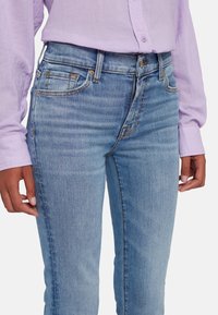 Jeans skinny azul claro con una textura suave, que presentan cinco bolsillos y detalles de costura sutiles, combinados con una camisa de manga larga lavanda.