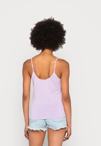 Top corto de color púrpura claro con tirantes delgados y ajustables y un escote redondo, combinado con pantalones cortos de mezclilla deshilachados, mostrando una textura de tela suave.