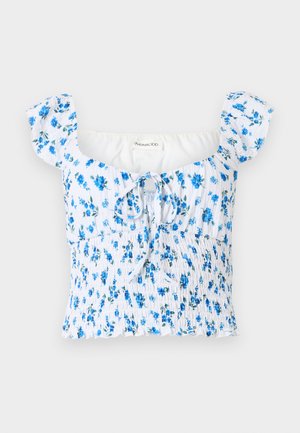 Haut court smocké blanc avec imprimé floral bleu, manches courtes bouffantes, encolure carrée et détail noué à l'avant.