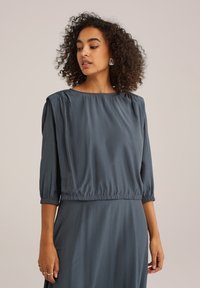 Robe bleu ardoise à manches trois quarts, épaules froncées et taille élastique. Texture lisse et design fluide.