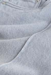 Gros plan sur un tissu denim gris clair avec des coutures visibles, des coutures et une partie du bord d'une poche.