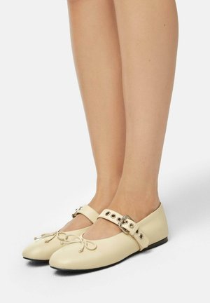 Ballet flats in cream leather with a rounded toe, bow detail, and an ankle strap featuring metal hardware and eyelet accents.