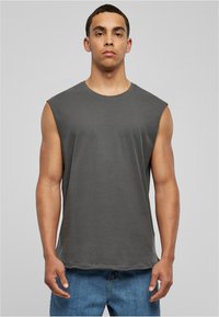T-shirt sans manches gris en coton. Encolure arrondie, coupe décontractée et texture subtile. Assorti à un jean en denim bleu clair.