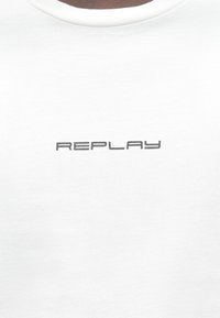 Camiseta de algodão branca com um logo "REPLAY" cinza impresso em uma fonte moderna no peito, com um clássico decote redondo.