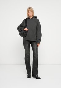 Haut en molleton oversized gris charbon avec une poche avant, associé à un jean gris foncé et des bottines noires à talons, tenant un sac noir.