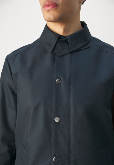 Navyblauer wasserdichter Mantel mit klassischem Kragen, ausgestattet mit silbernen Druckknöpfen, einer glatten Textur und einer vorderen Tasche für zusätzlichen Nutzen.