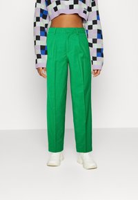 Gröna skräddarsydda byxor med framfållar, gjorda av ett slätt tyg. Stylad med en kort svart och lila rutmönstrad tröja och vita sneakers.