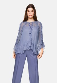 Lightweight, sheer, pastel blue blouse with ruffled edges and a tie-neck design. Paired with matching shiny slate blue trousers.