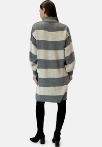 Stickad klänning med hög krage, med grå och krämfärgade horisontella ränder, lång ärm och sidslitsar vid fållen.