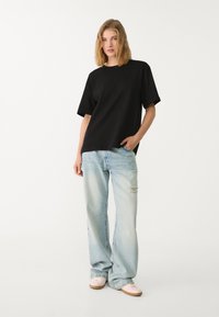 Sort oversized t-shirt, afslappet pasform, rund halsudskæring. Sammen med lyseblå slidte jeans og lyserøde low-top sneakers.