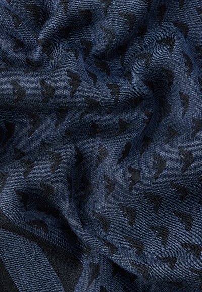 Μπλε ύφασμα με υφή υφαντού που παρουσιάζει ένα μοτίβο από μικρά, μαύρα, αφηρημένα βέλη διασκορπισμένα στην επιφάνεια.