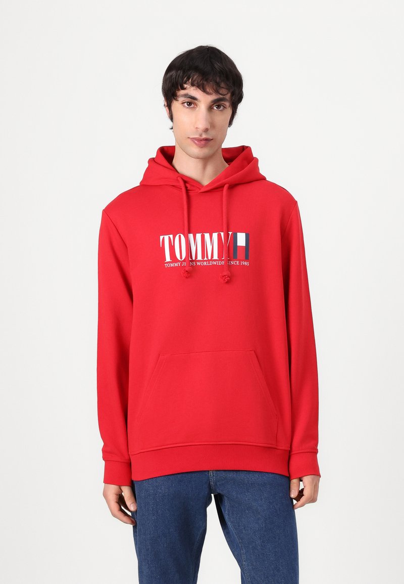 Felpa rossa con cappuccio realizzata in tessuto misto cotone. Presenta una tasca frontale a marsupio, cordini e un logo grafico sul petto.