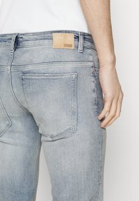 Vaqueros de mezclilla azul claro con una textura suave, diseño de cinco bolsillos y una etiqueta de piel con la inscripción "DRYKORN" en la cintura.