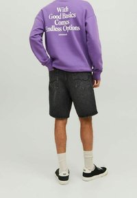 Felpa viola con testo bianco sulla schiena, abbinata a pantaloni corti di jeans neri. Sneakers nere e calze bianche alla caviglia completano l'outfit.