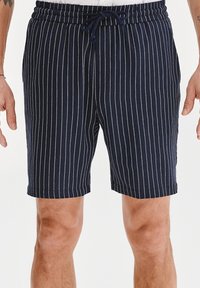 Granatowe szorty w białe pionowe paski, wykonane z lekkiego materiału, z elastycznym pasem i sznurkiem do regulacji dopasowania.