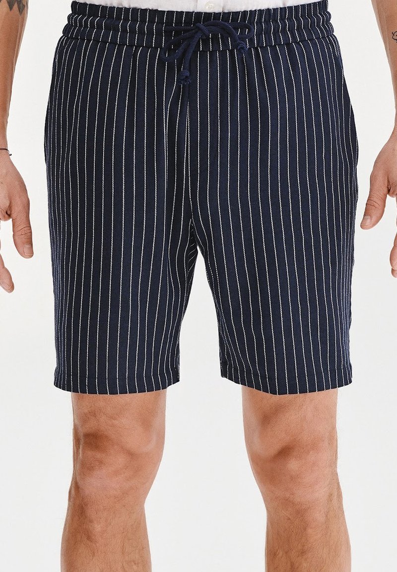 Granatowe szorty w białe pionowe paski, wykonane z lekkiego materiału, z elastycznym pasem i sznurkiem do regulacji dopasowania.