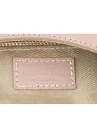 Lädermärke med präglad text "Gusti Leder" och "MADE IN ITALY," sydd på en beige tyginteriör med en fin gyllene dragkedjedetalj.