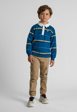 Polo rayé bleu à manches longues avec col blanc, pantalon cargo beige et baskets multicolores. Présente un logo sur la poitrine.