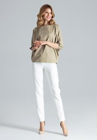 Beżowa, oversize'owa bluzka z rękawami 3/4, zestawiona z dopasowanymi białymi spodniami i beżowymi szpilkami, na szarym tle.