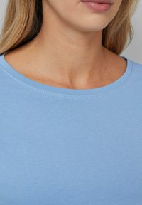 Light blue cotton t-shirt with a round neckline. Smooth texture and fitted design highlight the clean, simple style. Seam detailing visible.