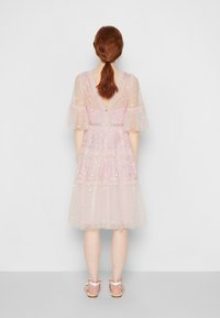 Robe en tulle rose avec des motifs floraux brodés, des manches évasées et un dos en V. Longueur genou avec des volants superposés.